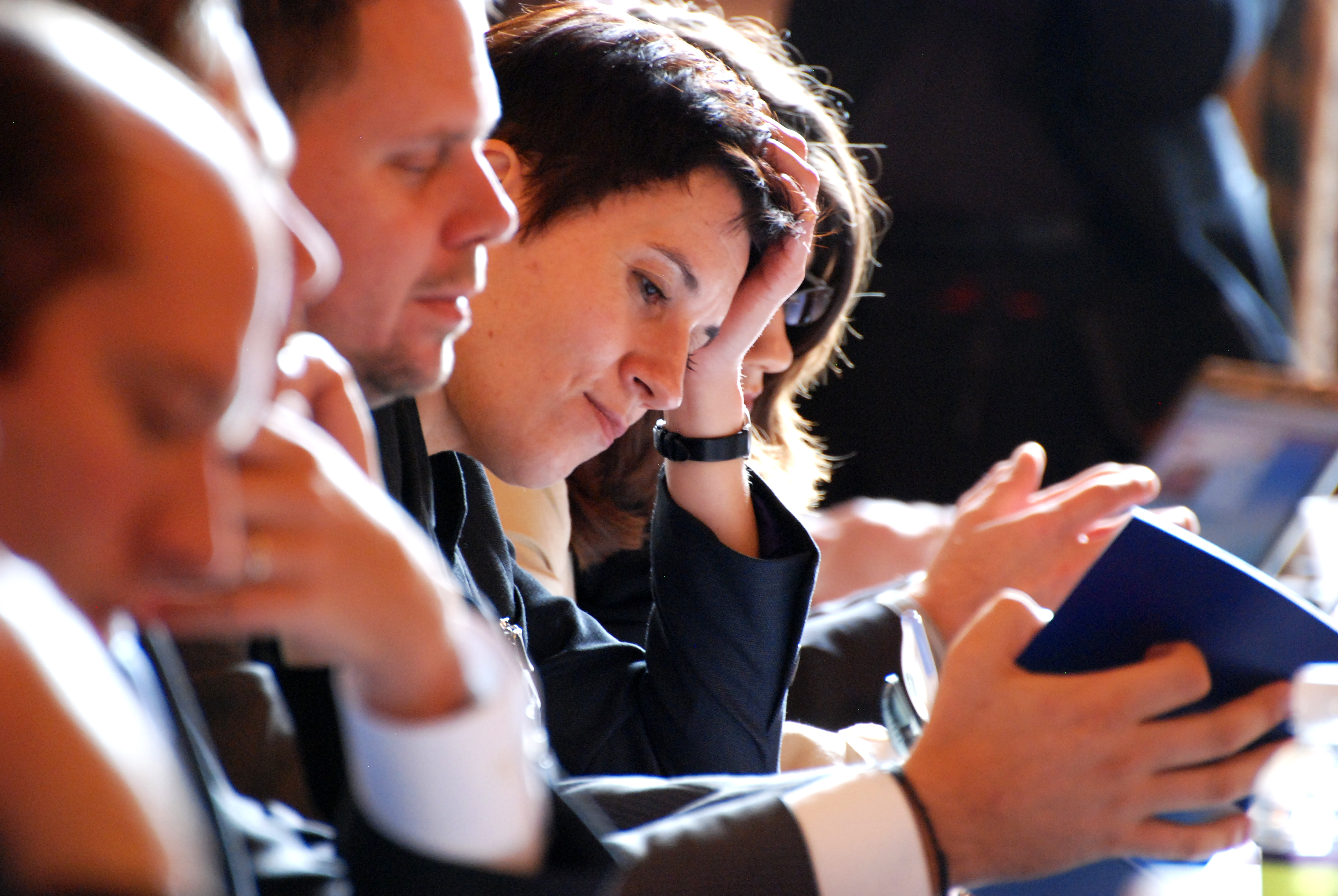 One of our photos taken at a cybersecurity conference in Washington DC, showing a woman reading and participants listening to speaker, sitting next to her at a conference table.